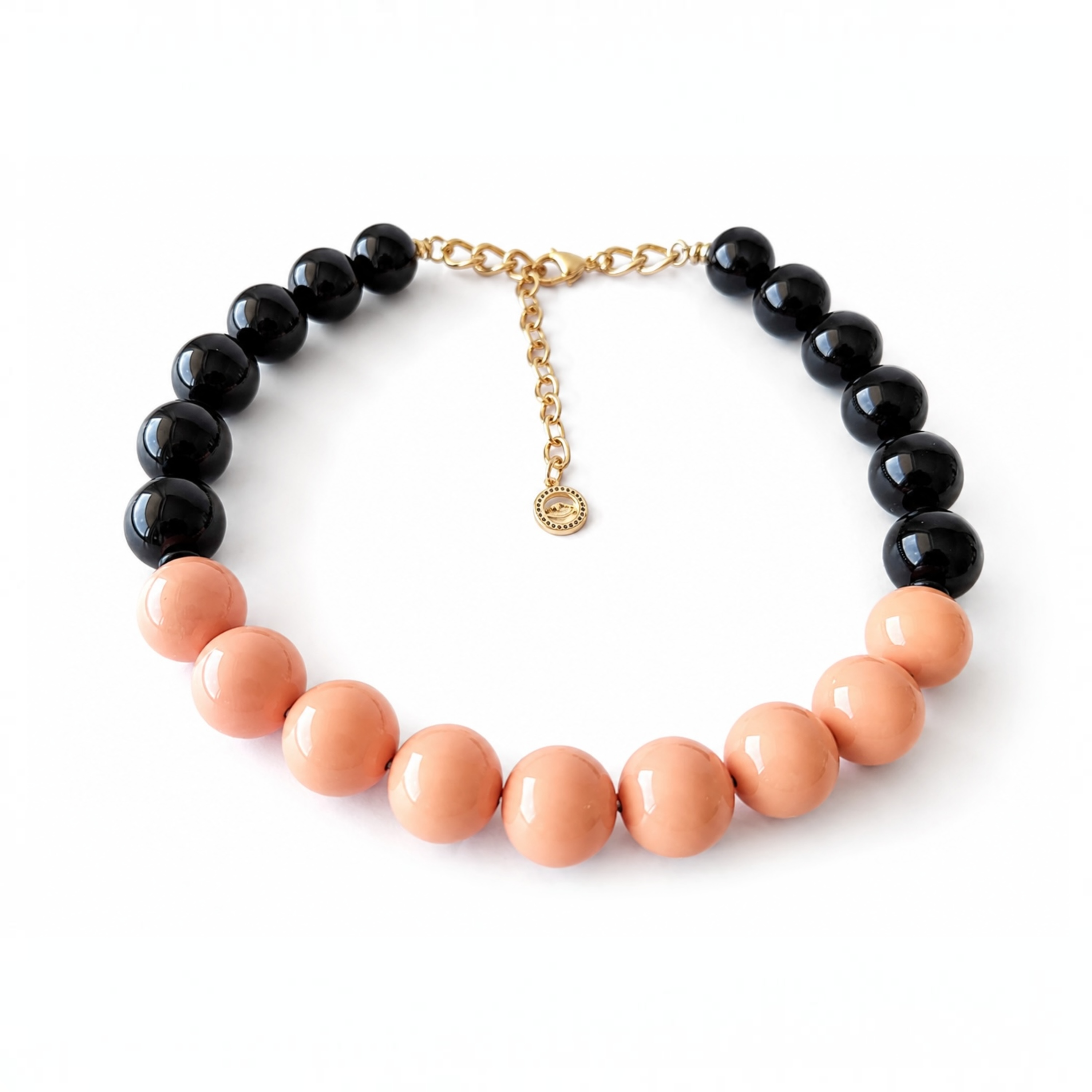 A beaded necklace with alternating glossy black and peach-colored round beads, connected by a gold-tone chain clasp with a small hanging charm, shown on a plain white background.