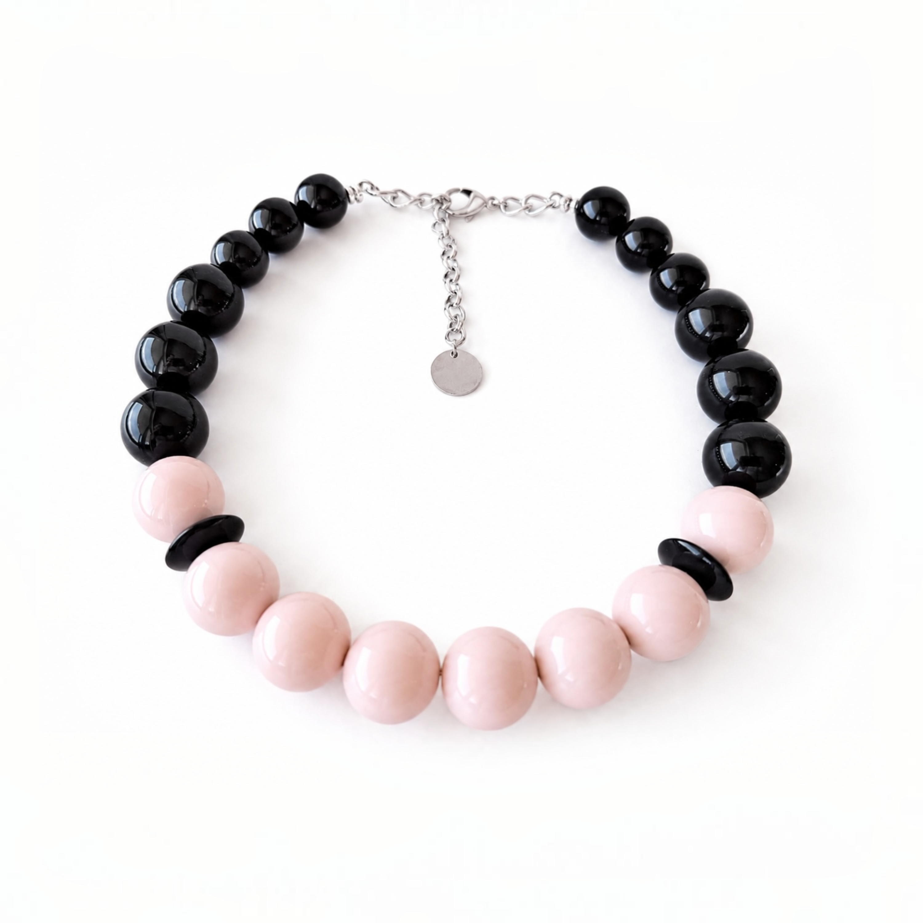 A beaded necklace featuring glossy black round beads and smooth pale pink round beads, arranged in an oval shape on a clean white background. A silver-tone clasp with a small round disc charm is visible at the top.